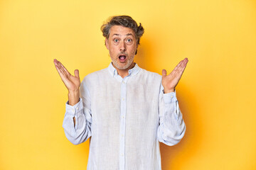 Wall Mural - Middle-aged man posing on a yellow backdrop surprised and shocked.