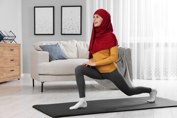 Wall Mural - Muslim woman in hijab stretching on fitness mat at home. Space for text