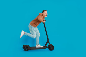 Emotional man riding modern electric kick scooter on light blue background