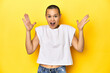 © Asier - Shaved head woman in white tank top, yellow backdrop celebrating a victory or success, he is surprised and shocked.