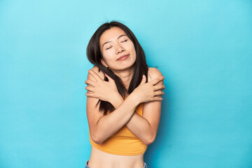 Wall Mural - Asian woman in summer yellow top, studio setup, hugs, smiling carefree and happy.