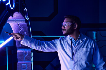 futuristic concept, indian scientist in goggles pointing with pen at new device in science center