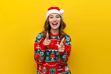 I Choose You. Young Girl In Christmas Sweater And Santa Claus Hat Smiles And Points At Camera On Yellow Background