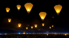 Handmade Paper Lantern Flying In The Night Sky Over Big City For Diwali Festival Of Lights Or Yi Peng Festival. Floating Lamp Balloons With Flame Inside Over The Town In India Or Thailand