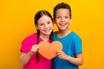 Wall Mural - Photo of good mood excited preteen schoolchildren wear t-shirts holding orange heart isolated yellow color background