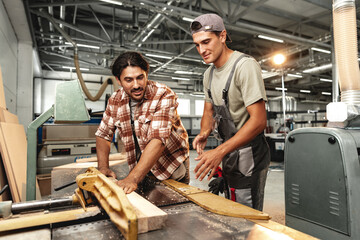 Wall Mural - Two young carpenters working with wood standing at table in workshop