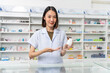 Happy beautiful asian female pharmacist wearing lab coat standing and holding pill bottle, She looking at camera feels good, trustworthy and proud of his work in the pharmacy drugstore.	