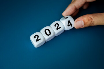 Poster - 2024 happy new year with change concepts. Close-up 2023 to 2024 year numbers calendar on white cube blocks flipping by human hand isolated on blue banner background.