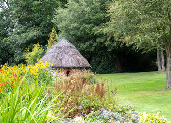 Wall Mural - Bressingham, Norfolk, UK – August 21 2023. Summer house with thatched roof in a tranquil and picturesque flower garden