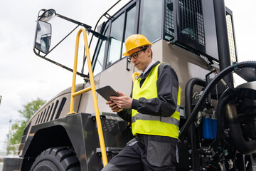 Poster - Engineer with tablet computer stands on the stairs to the cab of a truck.