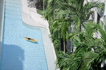 Wall Mural - Enjoying suntan. Tropical vacation concept. Top view of young woman on the yellow air mattress in the swimming pool with palm trees.