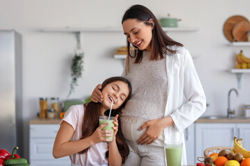 Wall Mural - Little girl with her pregnant mother drinking green smoothie in kitchen