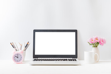 Wall Mural - Office workspace with laptop mockup screen, books, pink flowers in a vase, supplies on a light background. Home interior or office background