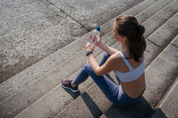 Wall Mural - Top view of exhausted fitness woman resting on concrete stairs after workout in city.