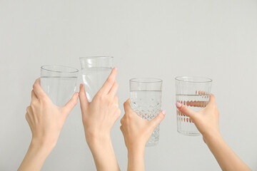 Wall Mural - Female hands with glasses of cold water on light background