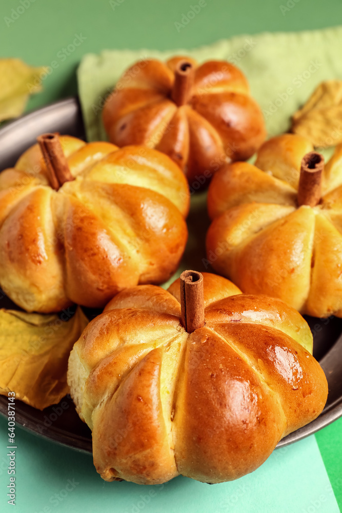 Plate with tasty pumpkin shaped buns on green background