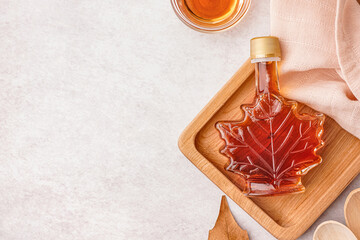 bottle of tasty maple syrup on light background
