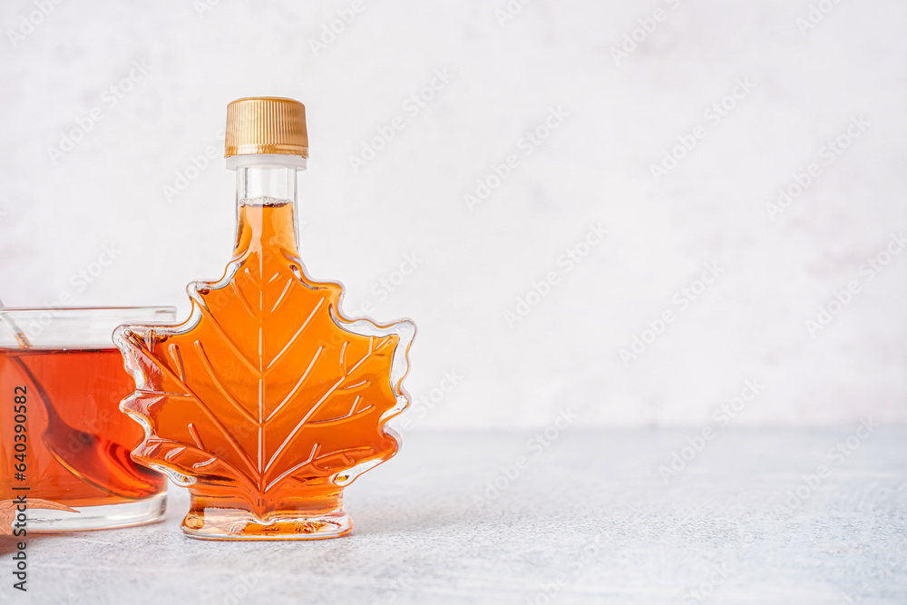 Bottle and glass of tasty maple syrup on table