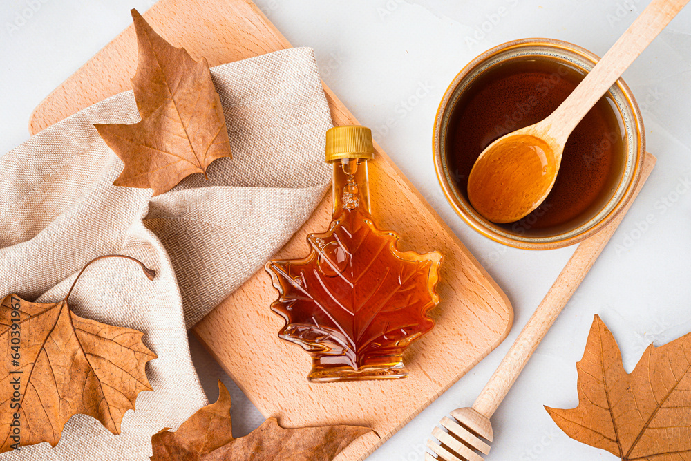 Bottle and bowl of tasty maple syrup on grey background