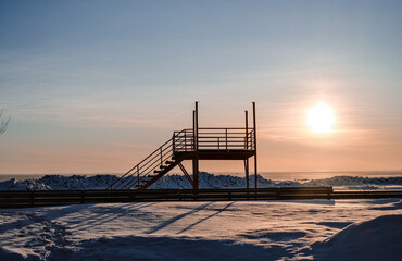 Wall Mural - Sunset in winter on a beach with a lot of snow and with a rescue post in the center