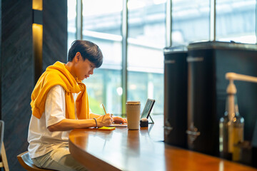 Young Asian man freelancer sitting in cafe working corporate business freelance job on digital tablet and mobile phone. Digital nomad people working from anywhere on gadget device and online network.