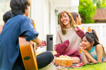 Group of young Asian woman enjoy and fun celebration meeting party at home backyard with playing guitar, singing, dancing, eating snack and drinking beer together on summer holiday festival vacation.