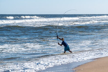 Young Fisherman Casting His Fishing Rod Into A Choppy Ocean With Heavy Swells On A Sunny Summer Day