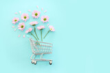 Fototapeta Mapy - Shopping cart with flowers over pastel blue background. Holidays shopping and sale concept