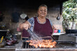 Latin poor woman cooking meat on a grill