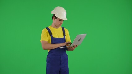 Medium green screen isolated chroma key shot of a young construction worker holding a laptop and typing, inserting data.