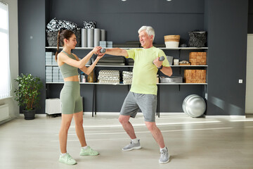 Wall Mural - Fitness instructor training senior man in health club, they exercising with dumbbells