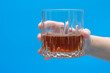 Szklanka z drinkiem, brązowym brandy, trzymana w dłoni 