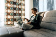 © Cavan Images - Woman uses laptop and smartphone sitting on couch in pajamas