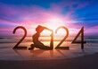 Happy new year card 2024. Silhouette of healthy girl doing Yoga One Legged Pigeon pose on tropical beach with sunset sky background, woman practicing yoga as a part of the Number 2024 sign.
