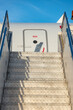 Looking up a set of aircraft access boarding stairs to a grey aircraft fuselage against a blue sky, vertical