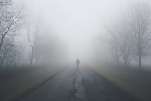 Silhouette Of Man Who Walking Alone In Foggy Autumn Or Winter Asphalt Road Rear View. Loneliness And Melancholy Concept.