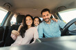 © Prostock-studio - Happy european family with child girl sitting inside car and smiling at camera, enjoying road trip in new automobile