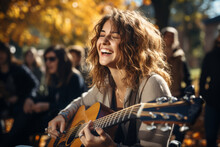 Cheerful Young Female Musician Performing For Her Fellow Hikers On Sunny Fall Day. Performer Playing A Guitar In The Wild. People Having Fun On A Hike In Autumn.