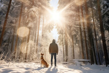 A Man And His Pet Dog Walking Though A Snowy Forest On Sunny Winter Day. Adventurous Young Man And His Dog On A Walk. Hiking And Trekking On A Nature Trail. Traveling By Foot.