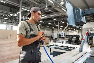 Wall Mural - Young carpenter operating machine for wood processing at a furniture factory