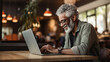 © Concept Island - Older black man using his laptop computer at a coffee shop table. Older people and technology.