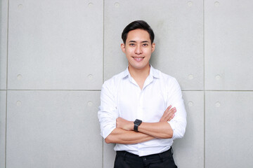 Portrait of an Asian man working in an office standing with his arms crossed and smiling happily. Businessman concept.