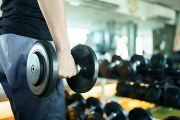 Active Asian sportsman doing a weight exercise in a gym - fitness by lifting up a dumbbell, man lifting up or holding a heavy dumbbell from dumbbell rack.