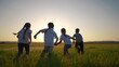 © maxximmm - a group of children run across the field on the grass. happy family kid dream concept. children running in a field lifestyle with tall grass. girls holding hands in the foreground on the sunset