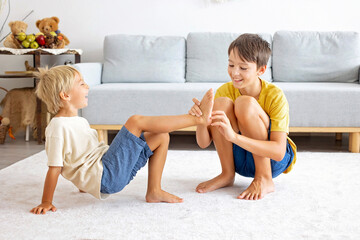 Wall Mural - Happy positive children, tickling on the feet, having fun together, boy brothers at home having wonderful day of joy