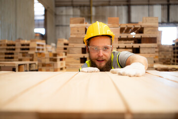 A guy carpenter in a hardhat and glasses inspects a completed work item at a timber industry.