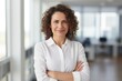 © id512 - a confident Latin middle-aged businesswoman stands in her office with her arms crossed, looking directly at the camera for a portrait