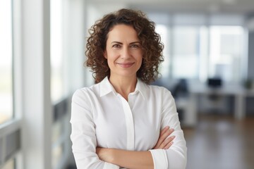 a confident Latin middle-aged businesswoman stands in her office with her arms crossed, looking directly at the camera for a portrait