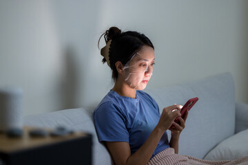 Poster - Woman use cellphone and apply the paper mask on face at home in the evening