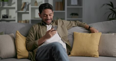 Young man with surprised face looking at smartphone while sitting on the sofa.